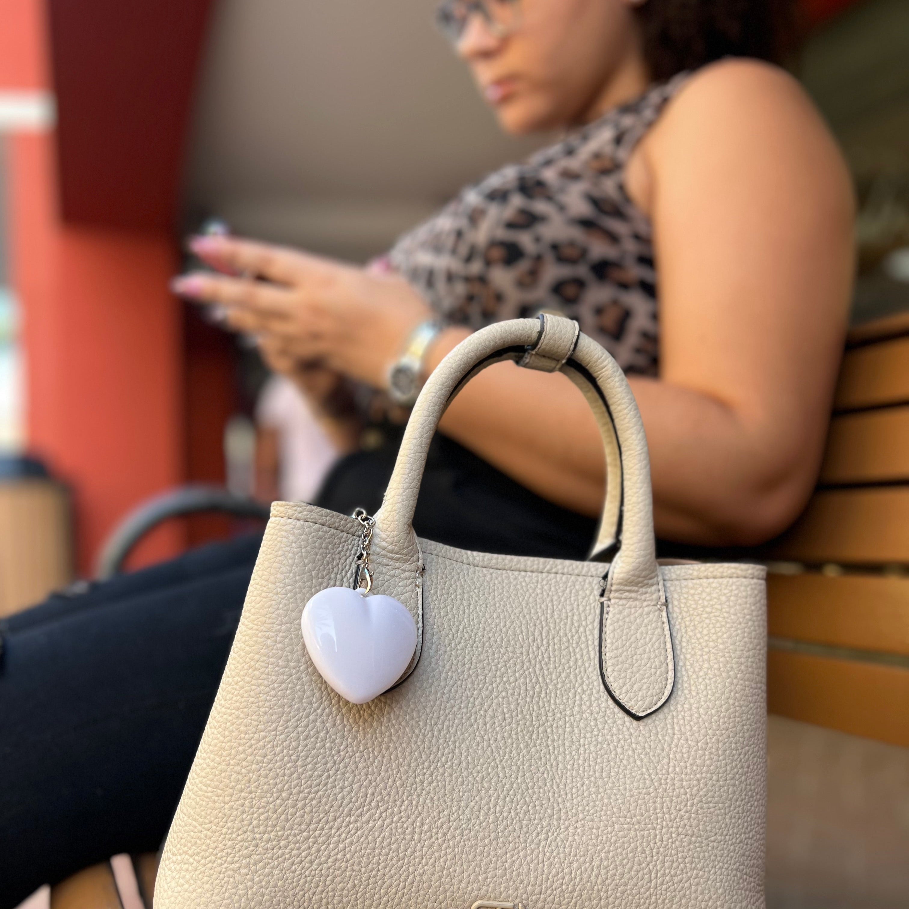 Beige handbag with a heart-shaped charm on a wooden bench, blurred background